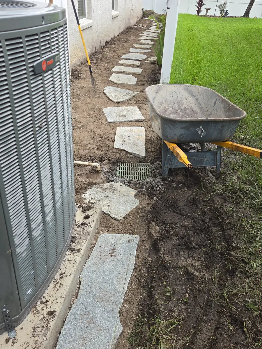 Flagstone stepping stones being set over a new French drain beside an AC unit in a Tampa Bay FL side yard by Living Spaces Gardening