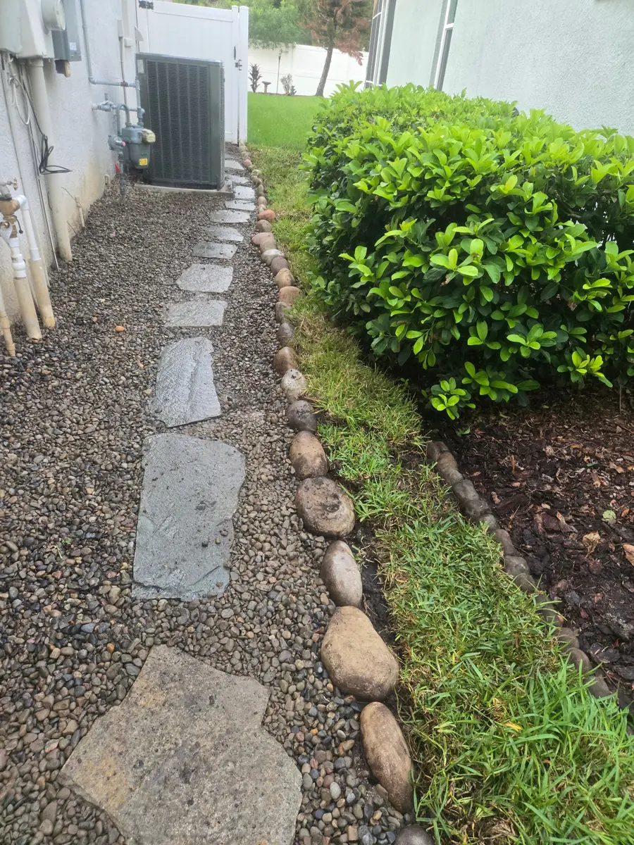 Finished side yard with flagstone path in river rock, stone edging, and native shrubs by Living Spaces Gardening in Tampa Bay FL